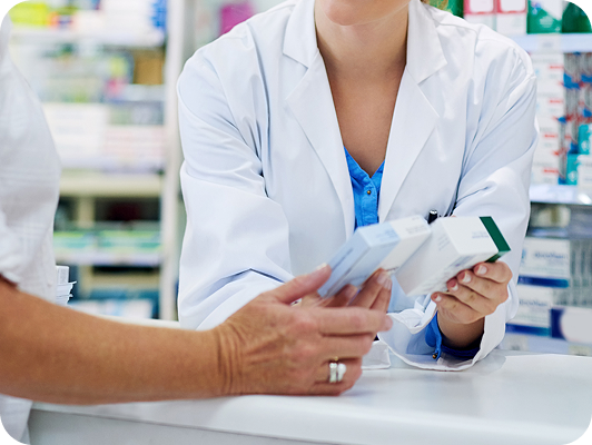 Due professioniste in camici bianchi controllano scatole di medicine in una farmacia, primo piano su mani e confezioni.