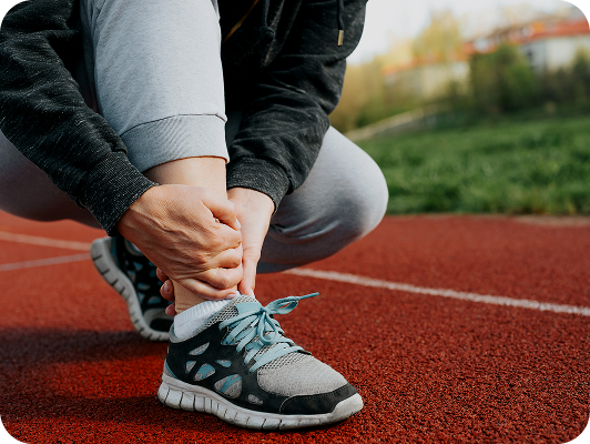 Persona che si tiene la caviglia su una pista di atletica rossa, contesto all'aperto.