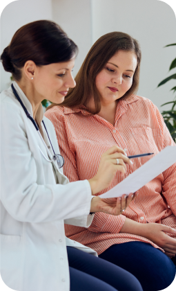 Due donne: una medico in camice bianco consulta una paziente in camicia a righe, esaminando documenti medici.