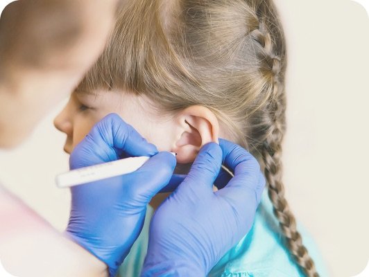Donna con guanti blu esamina l’orecchio di una bambina durante un controllo medico