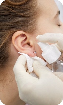 Prima infusione innocua: medico usa spray disinfettante vicino allorecchio di una paziente, primo piano su orecchio e guanti chirurgici.