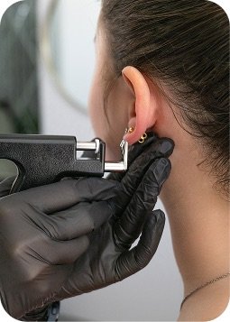 Procedura di piercing all'orecchio con strumenti, mani guantate e orecchio della cliente in primo piano