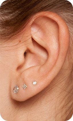 Orecchio femminile con tre orecchini a pietre incastonate: due piccole e una più grande, in argento.