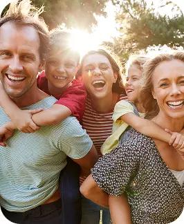 Famiglia felice all’aperto, abbracci stretti tra risate, sole sullo sfondo e atmosfera gioiosa.