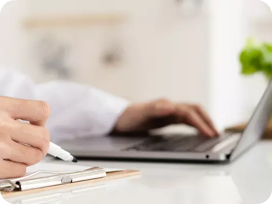 La mano di una persona scrive su una penna e lavora su una tastiera di laptop su una scrivania luminosa.