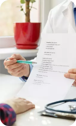 Medico illustra un documento con penna verde, evidenziando un elenco di voci sul foglio durante la visita.