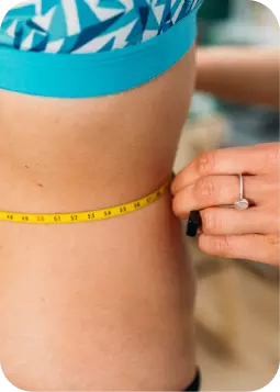 Donna in costume da bagno durante una misurazione con nastro giallo intorno alla vita, evidenziando la silhouette.