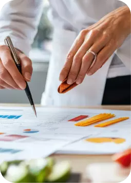 Nutrizionista lavora su grafici: una mano tiene una penna e l’altra una gomma, con grafici colorati sul tavolo.