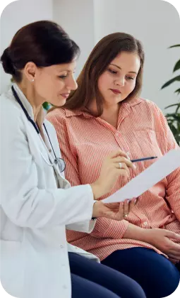 Due donne: una medico in camice bianco consulta una paziente in camicia a righe, esaminando documenti medici.
