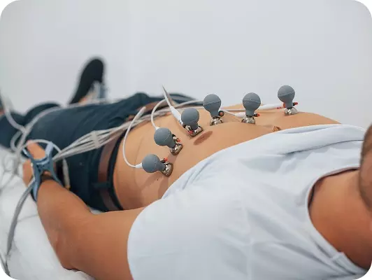 Persona distesa su lettino, con elettrodi per elettrocardiogramma sull'addome, monitoraggio medico in corso durante esame.