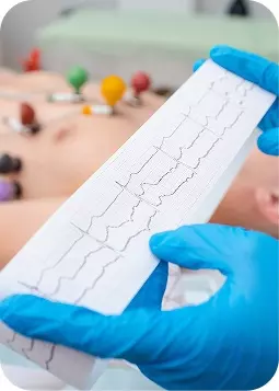 Ecografia cardiovascolare su schermo con operatore in guanti blu, primo piano su elettrodi e paziente disteso.