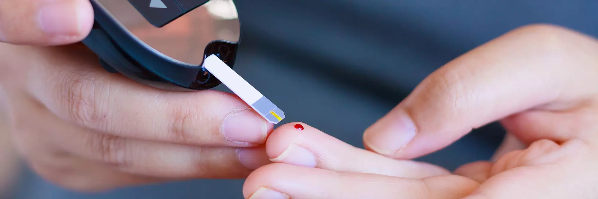 Primo piano su strumento che misura la glicemia con una piccola striscia lanciata sul dito, evidenziando un punto di sangue.