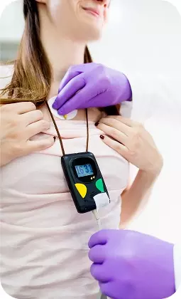 Donna controlla i battiti con un holter cardiaco portatile, mentre un medico indossa guanti viola.