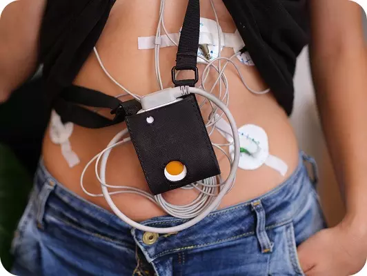 Holter cardiaco e pressorio con monitoraggio medico attaccato all’addome, cavi e sensori visibili su pelle abbronzata