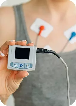 Donna che tiene un monitor cardiaco portatile con elettrodi attaccati al petto.