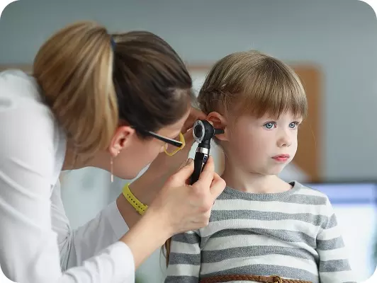 Medico controlla orecchio a un bambino in età scolare con otoscopio, ambiente ospedaliero o clinico.