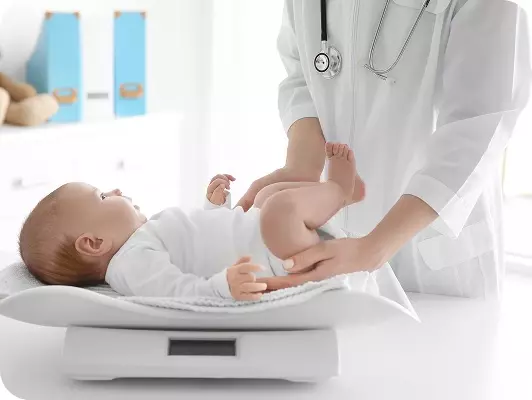 Pediatra in camice con stetoscopio controlla il peso di un neonato sdraiato su una bilancia pediatrica