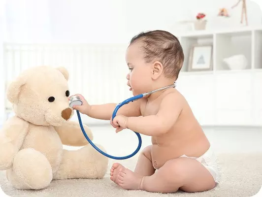 Bambino che gioca al medico con un enorme orso di peluche usando uno stetoscopio blu in una stanza luminosa.