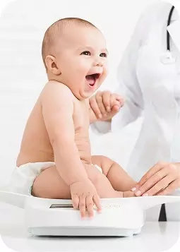 Neonato felice in controllo medico, seduto sul fasciatoio mentre un medico in camice controlla il peso e la salute del bambino.