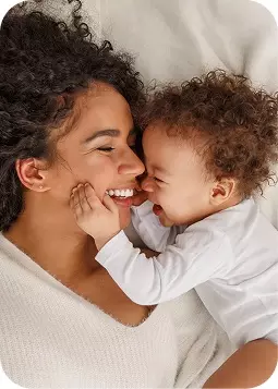 Donna sorridente con un bambino che tocca le sue guance, momento tenero di affetto familiare.