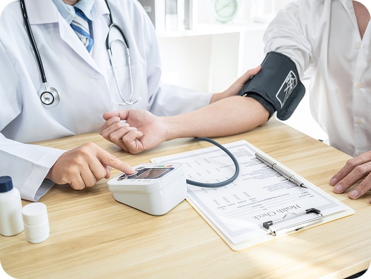 Medico con stetoscopio esamina pressione sanguigna del paziente usando misuratore automatico, documentazione clinica sul tavolo.