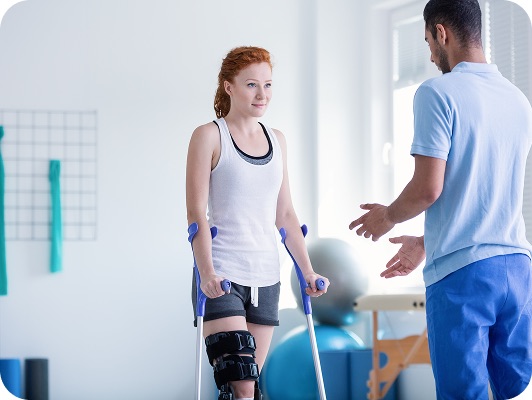 Donna su stampelle durante una sessione di riabilitazione, allenatore al fianco in palestra luminosa.