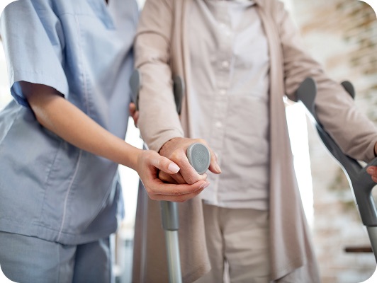 Operatore sanitario assiste persona anziana con le stampelle, mani unite per sostegno e camminamento assistito.
